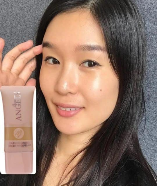 Mujer sosteniendo un tubo de producto, sonriendo, sobre un fondo gris.