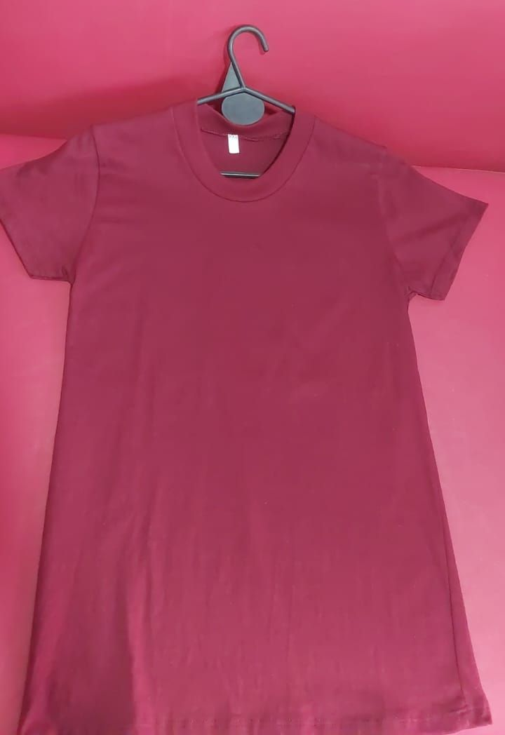 Camiseta granate colgada en una percha negra sobre un fondo rosa.