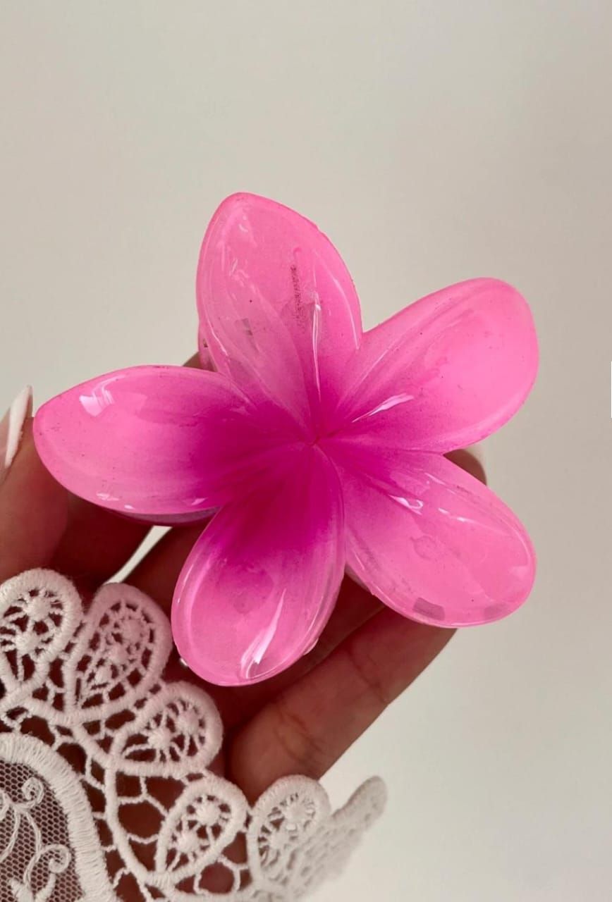 Pinza para el cabello rosa con forma de flor sostenida por una mano con una funda de encaje blanco.