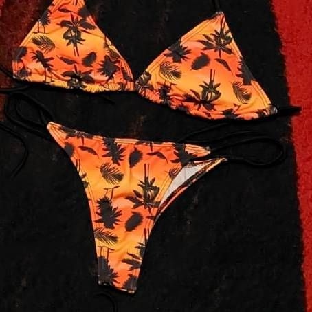 Bikini naranja con estampado de palmeras negras sobre fondo negro.
