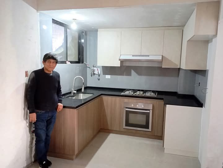 Un hombre está de pie en una cocina al lado de un fregadero y una estufa.