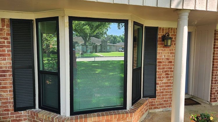 Bay window with black trim and shutters on a brick house.