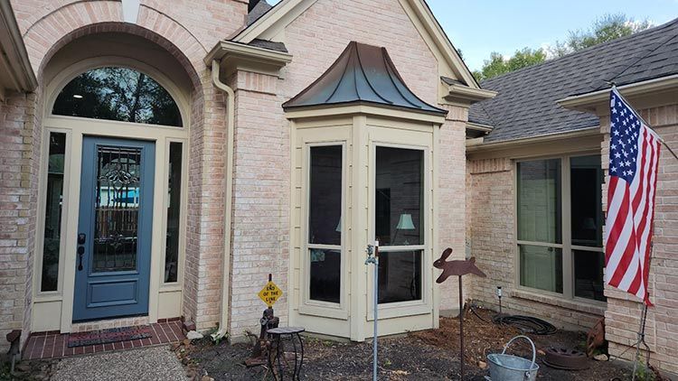 Tan brick house with a blue door, arched entryway, and a small bay window. American flag is displayed.