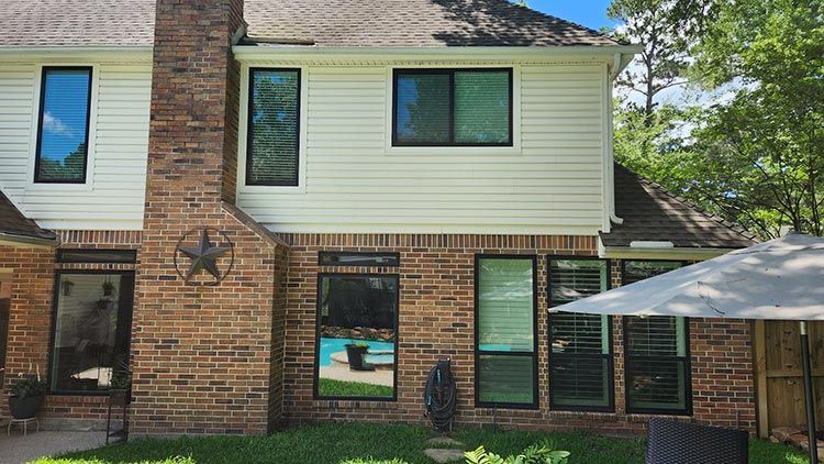 Back of a two-story house with brick chimney, white siding, black-framed windows, and a patio umbrella.