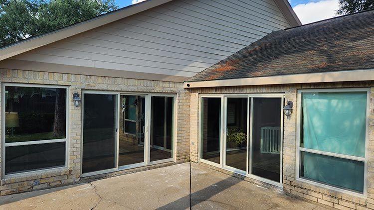 Exterior view of a house with sliding glass doors, brick walls, and a concrete patio.