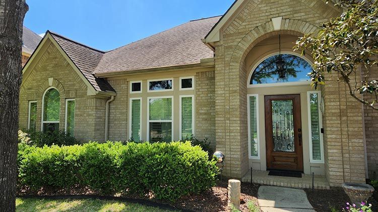Tan brick house with arched doorway, several windows, and manicured shrubs.