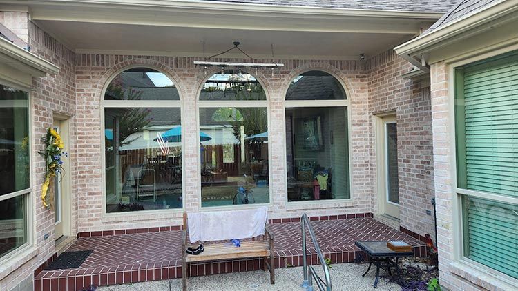 Covered patio with arched windows overlooking a pool area; brick facade, bench, and small table.