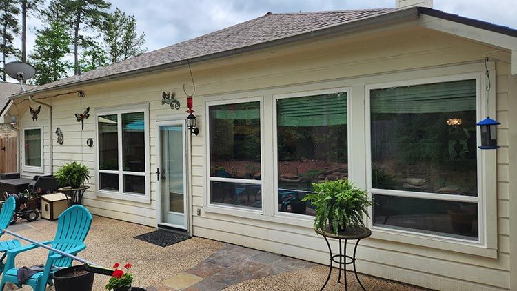 Back patio of a house with light yellow siding and large windows, a door, and patio furniture.