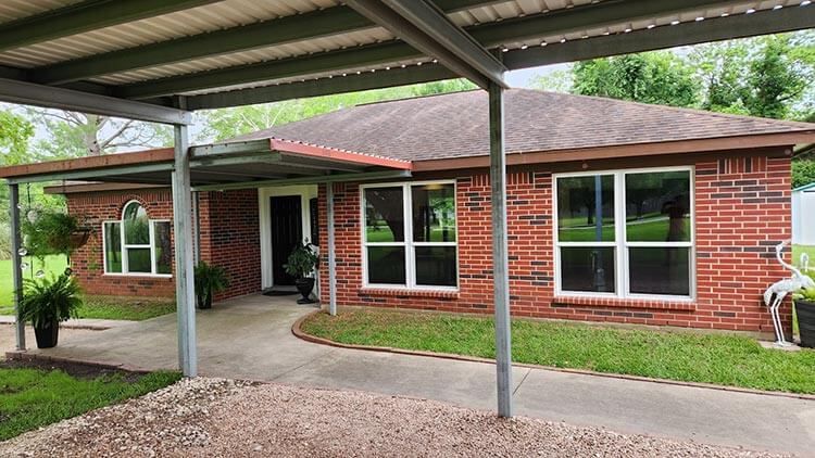 Brick house with a covered carport, pathway, and landscaping.