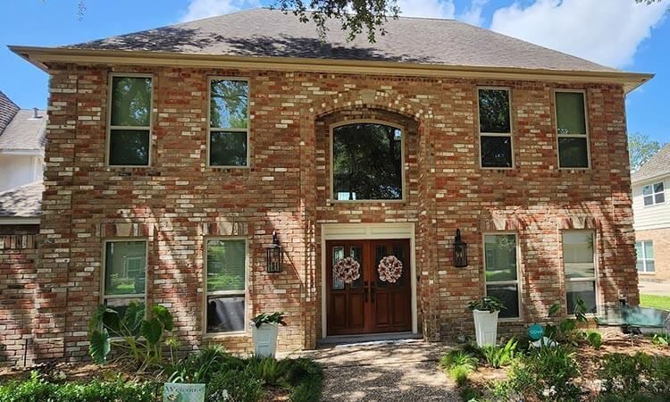 Two-story brick house with multiple windows and double wooden doors.