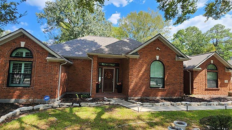 Red brick house with arched windows, door, and grey roof under a blue sky.