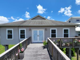 Wooden building with a walkway, light-colored siding, and a deck. Blue sky with clouds overhead.
