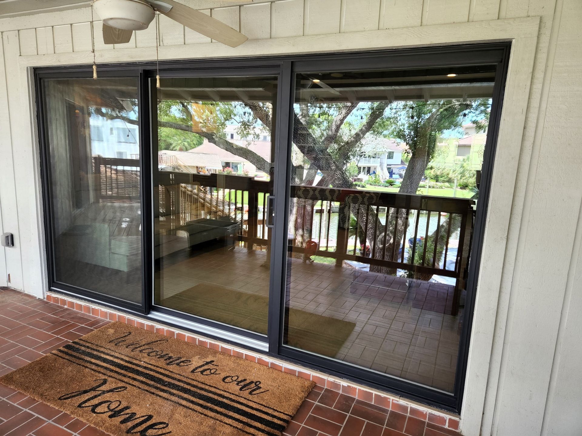 Sliding glass doors open to a deck with a tree view. A doormat says