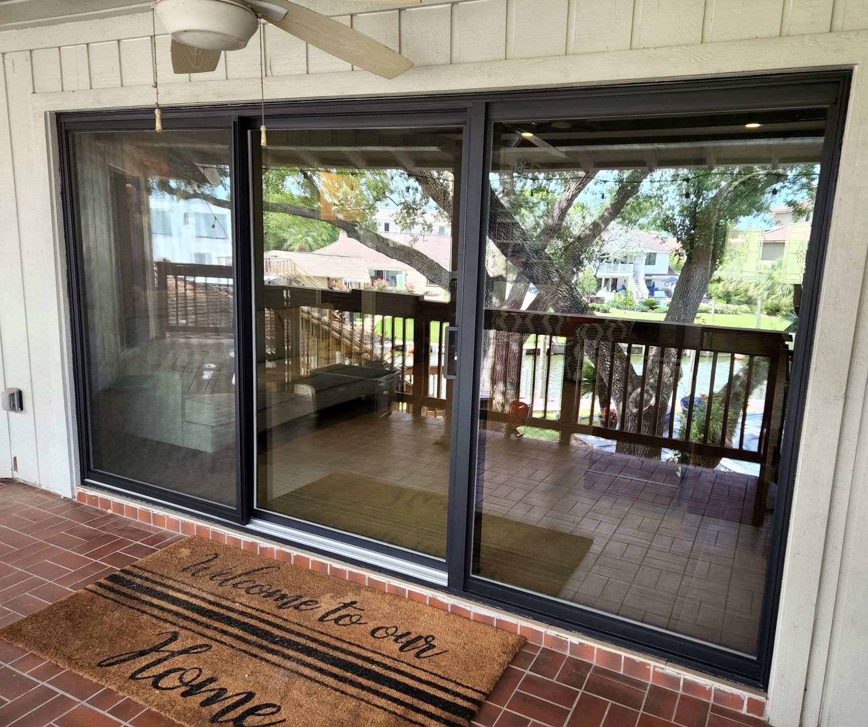Sliding glass doors open to a deck with a tree view. A doormat says
