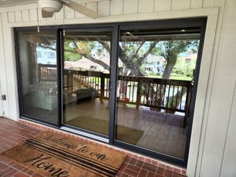 Sliding glass doors open to a deck with a tree view. A doormat says