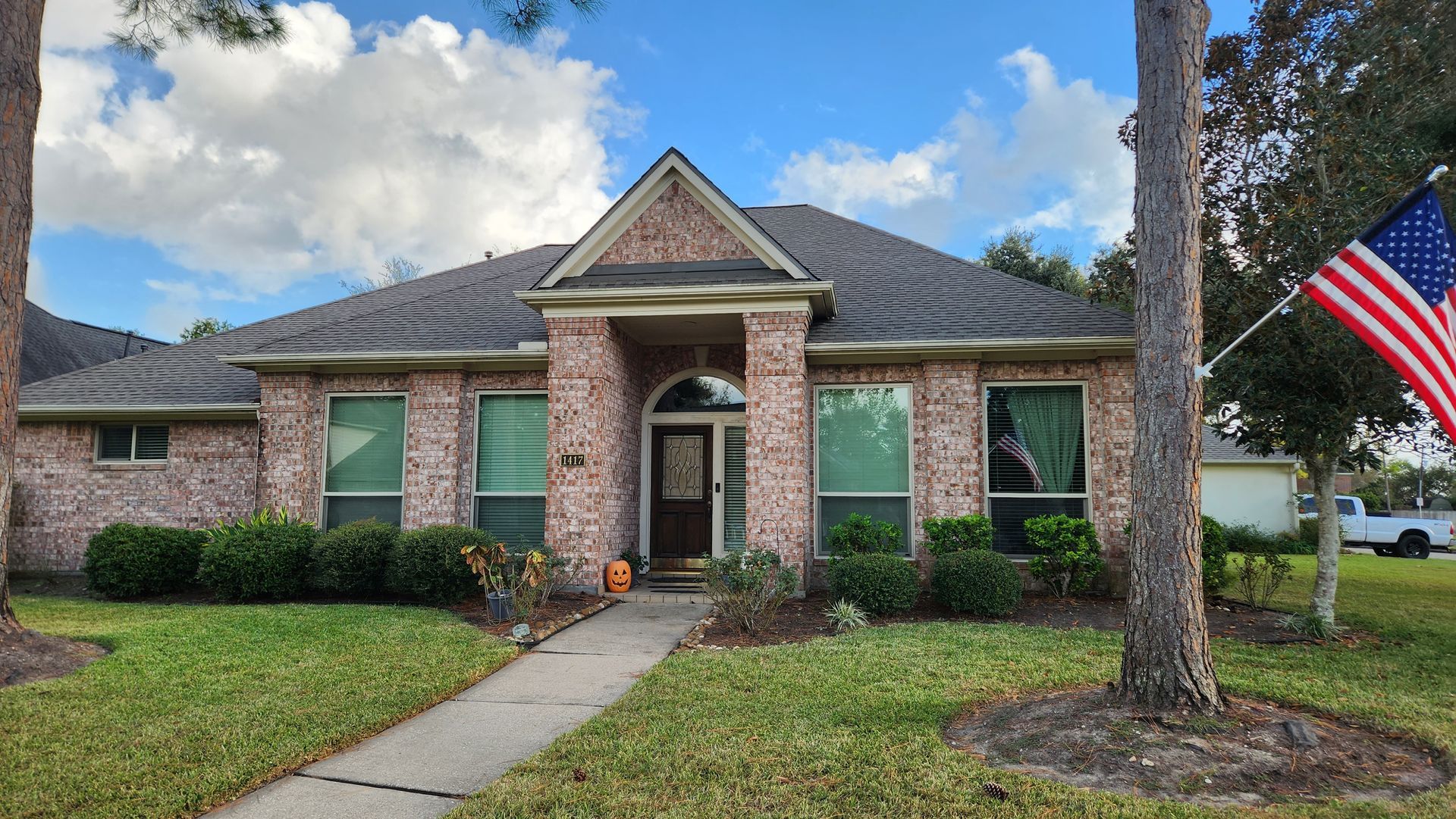Tan brick house with arched doorway, several windows, and manicured shrubs.