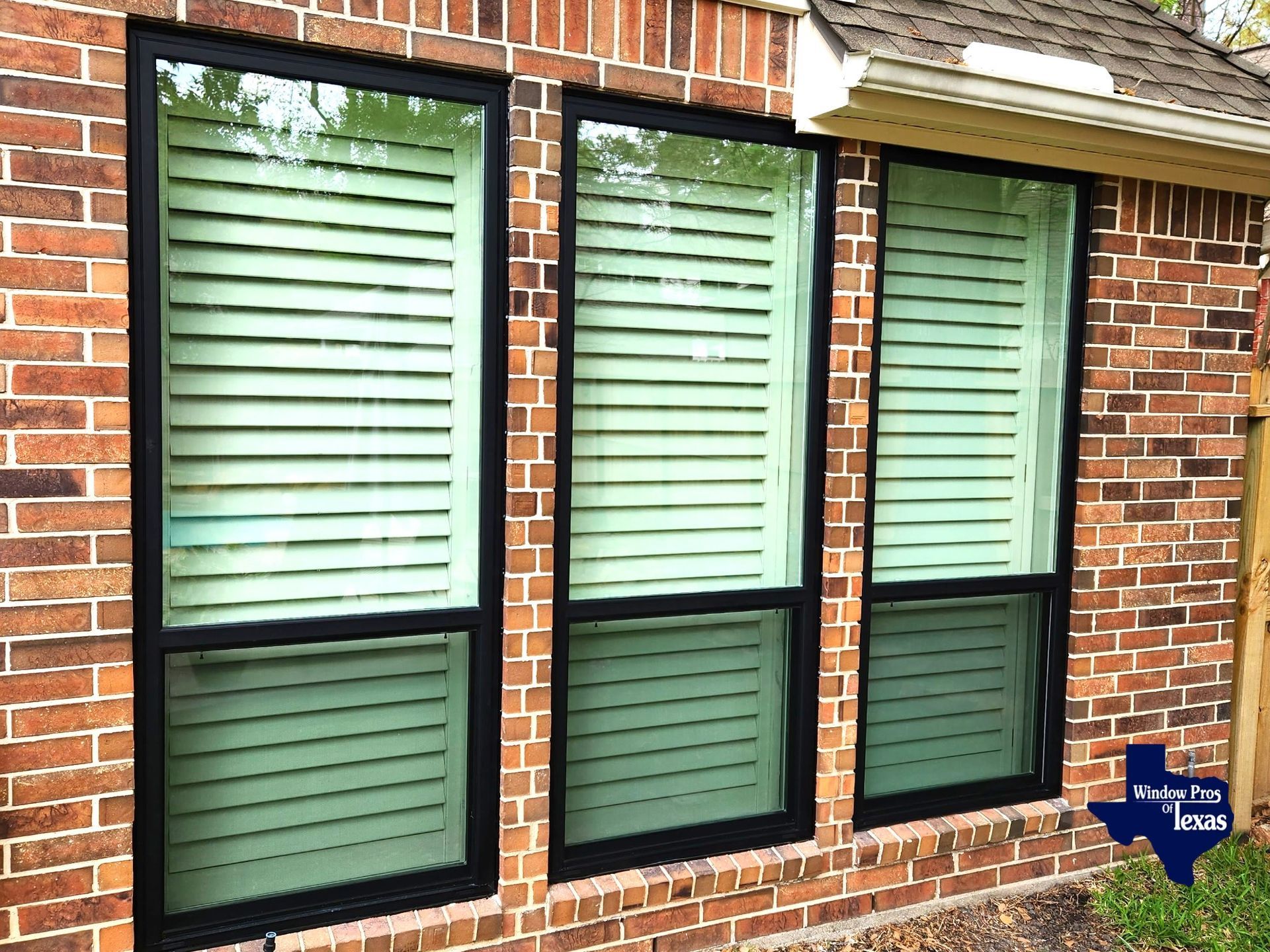 Three windows with light-colored slatted blinds in a brick building. Black window frames.