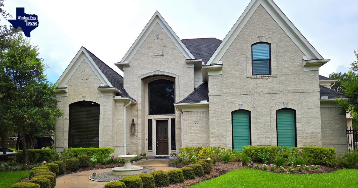 Two-story brick house with dark roof and green shutters. Small fountain and well-manicured lawn in front.