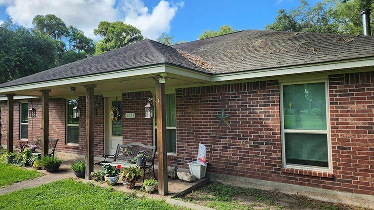Brick house with a porch, green lawn, and a cloudy blue sky.