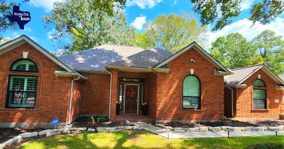 Red brick house with arched windows and a gray roof, set among trees on a sunny day.