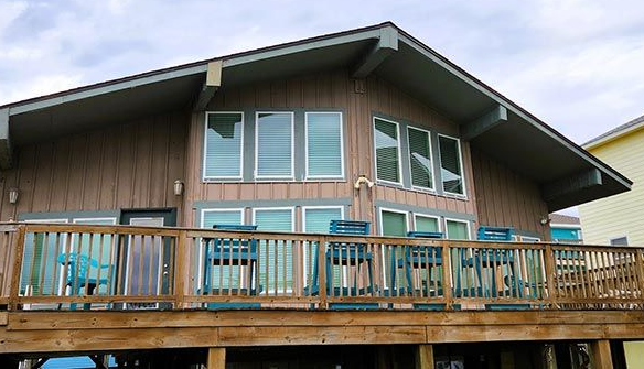 Beach house with wood siding, deck, and large windows under cloudy sky.
