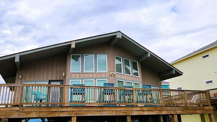 Beach house with wood siding, deck, and large windows under cloudy sky.