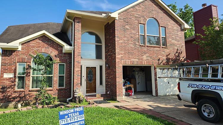 Two-story brick house with large windows, garage, and service truck parked in driveway.