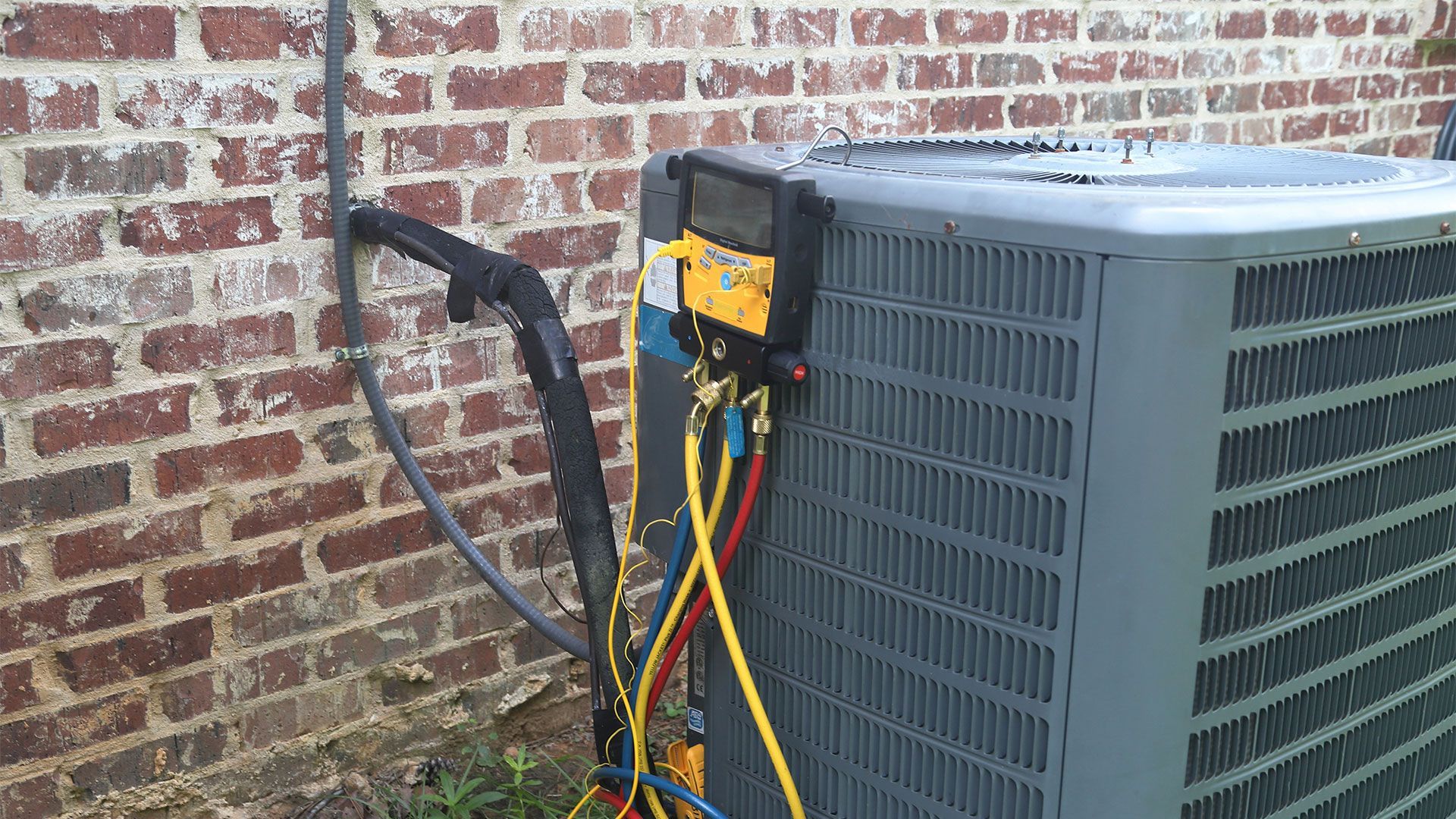 An air conditioner is being installed in front of a brick wall.