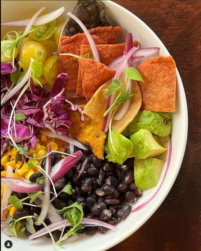 Un tazón blanco lleno de una variedad de verduras y patatas fritas.