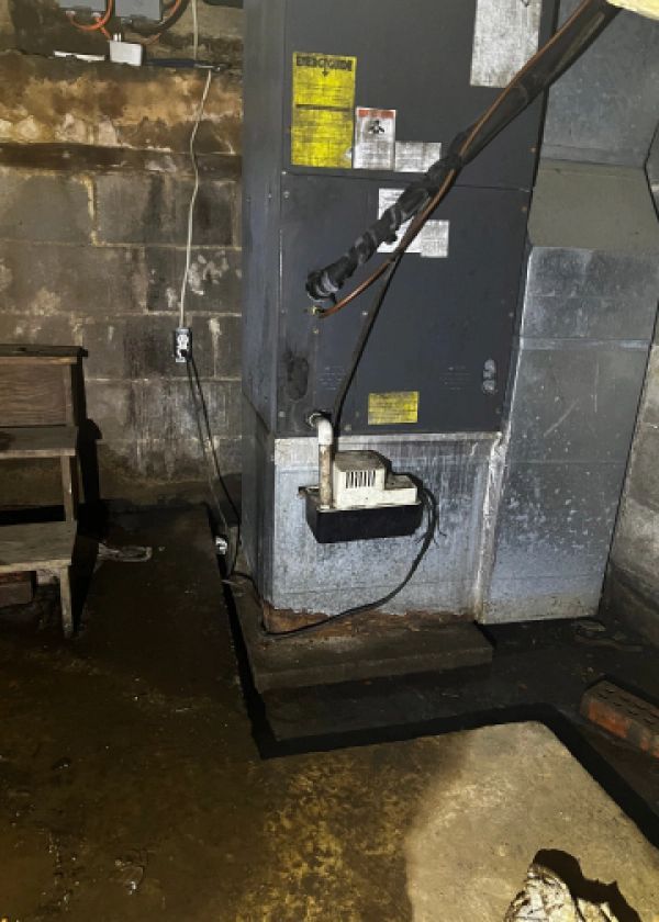 A furnace is sitting in a basement next to a brick wall.