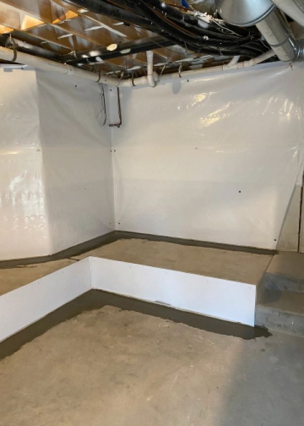 A corner of a basement with a white wall and a concrete floor.