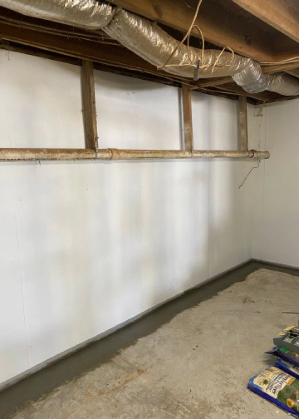 A basement with a white wall and a bag of dirt on the floor.