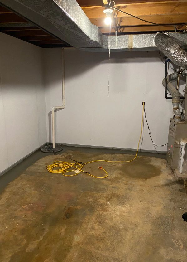 An empty basement with a heater and a yellow cord.