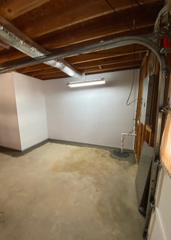 An empty basement with a garage door open and a light on the ceiling.