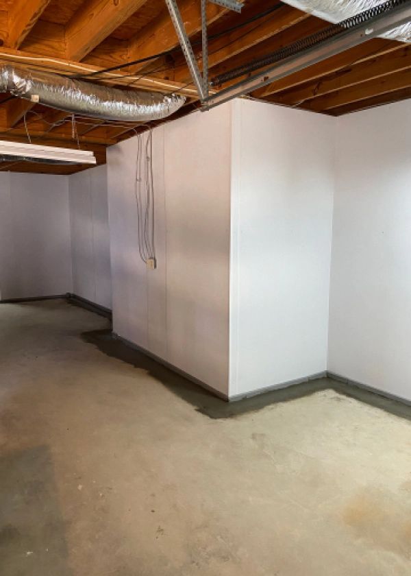 An empty basement with white walls and a wooden ceiling.