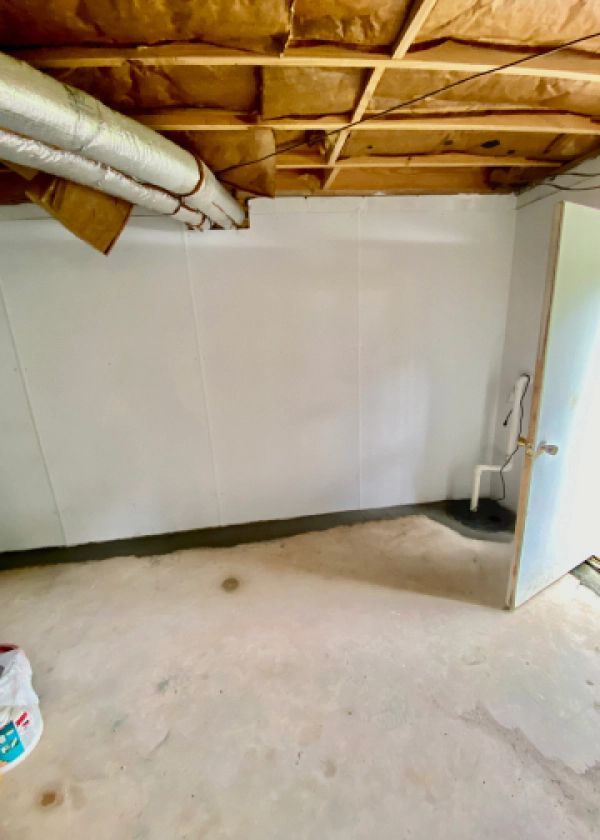 A basement with a white wall and a door.