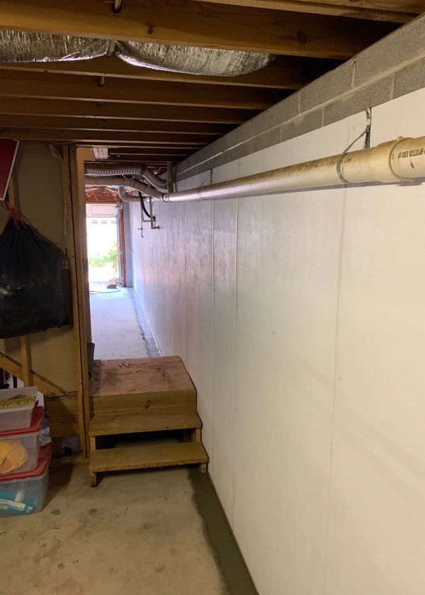 A basement with a white wall and stairs leading to a garage.