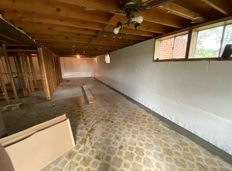 An empty basement with a ceiling fan and a brick wall.