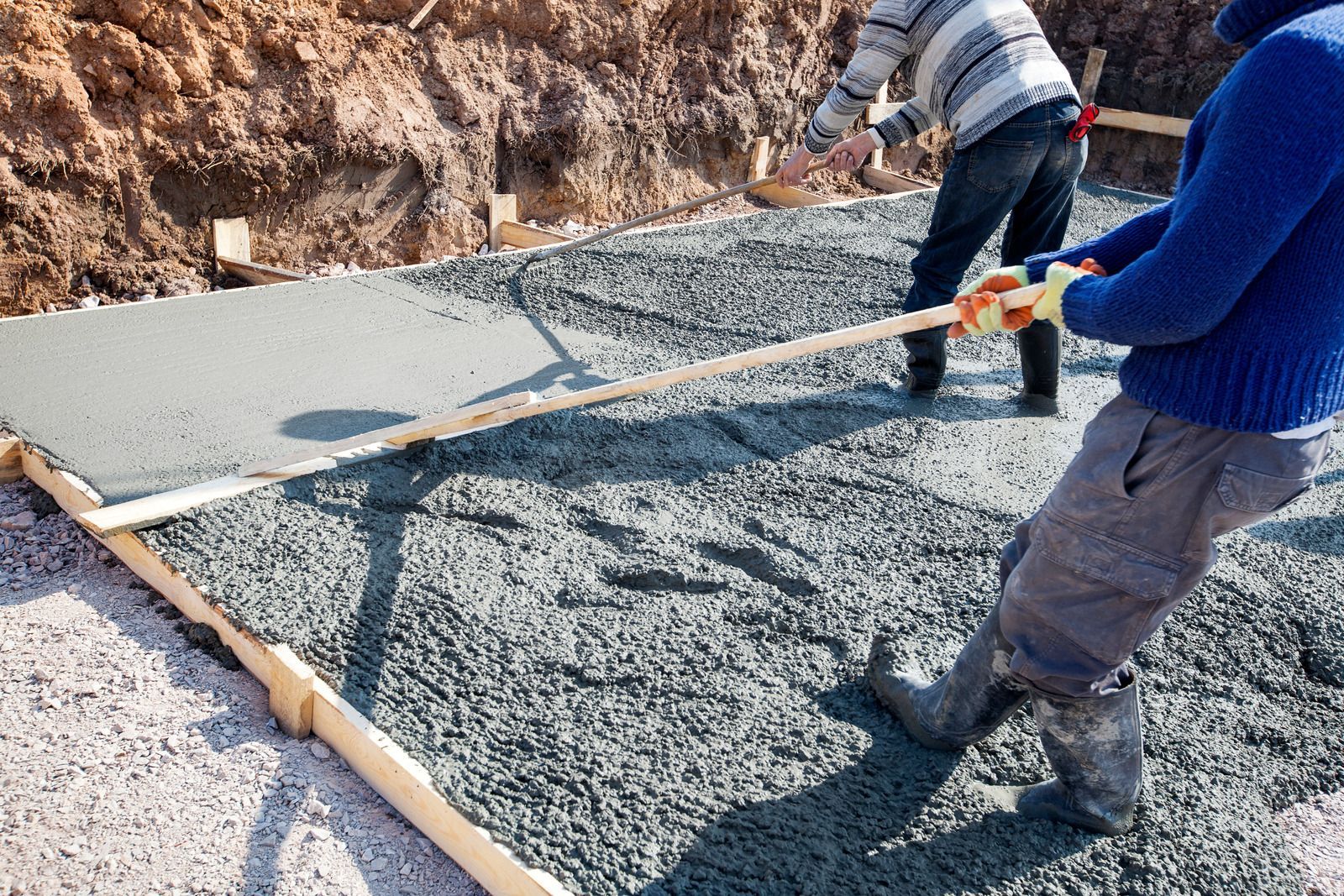 Construction workers leveling wet concrete in a wooden frame, outdoors.