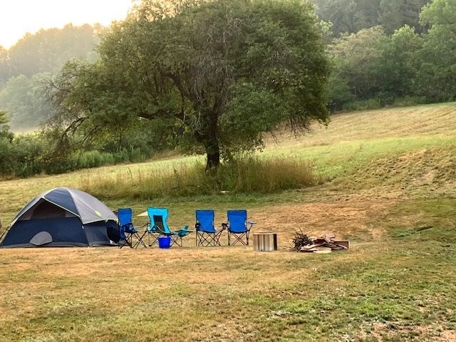 A tent , chairs and a fire pit in a field.