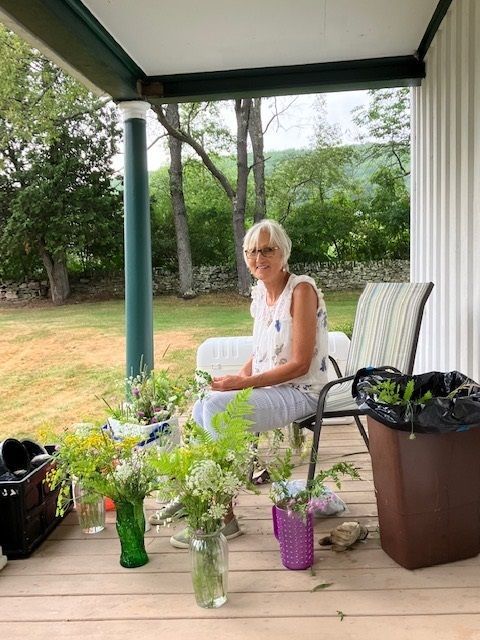 A woman is sitting on a porch with flowers in vases.