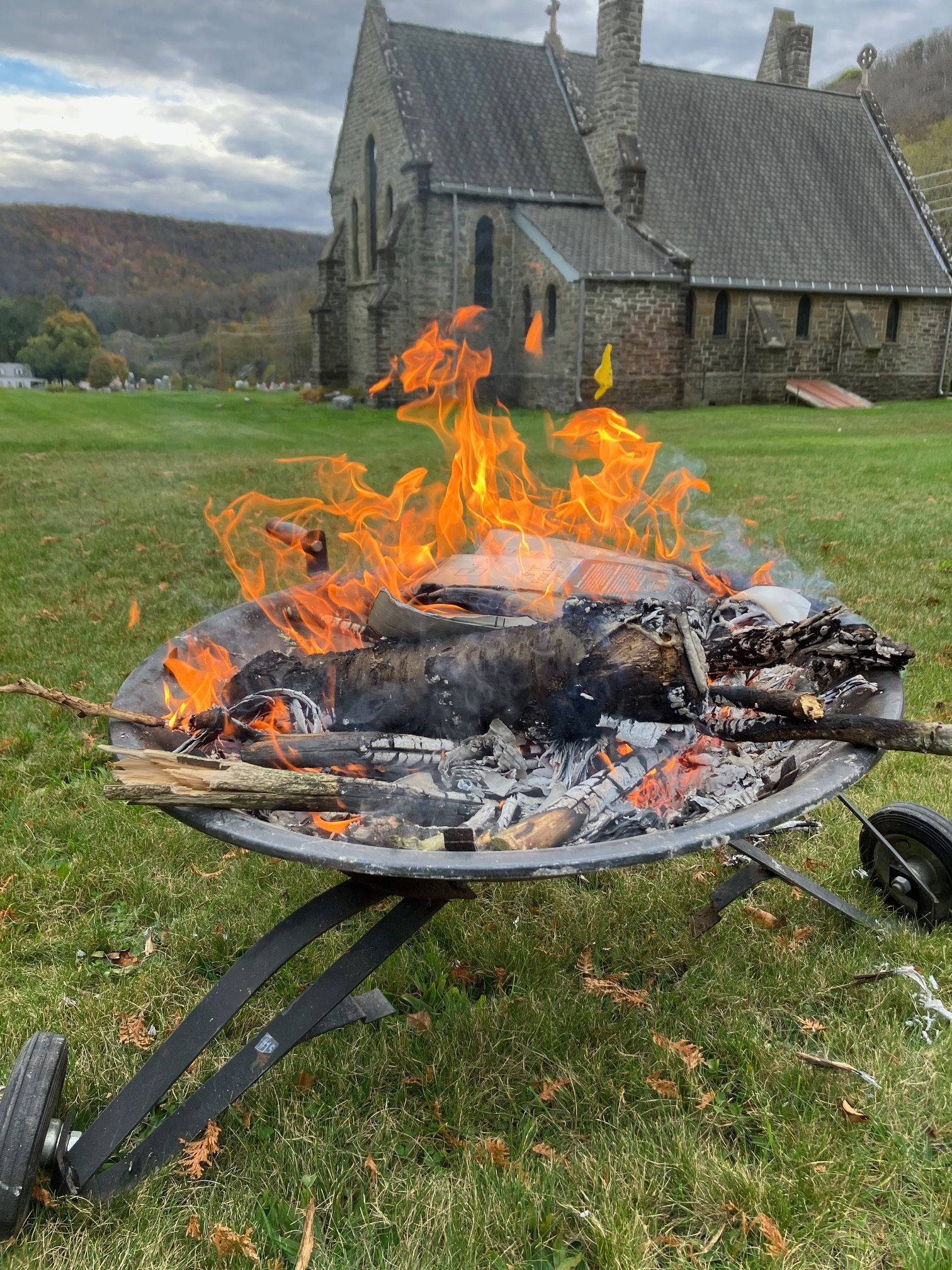 A fire pit in a field with a church in the background