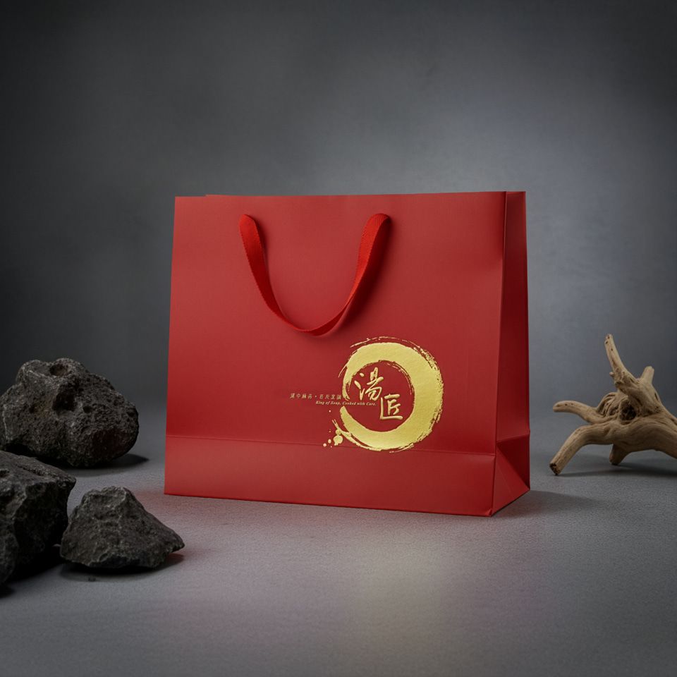 一個紅色購物袋，帶有金色標誌和提手，放在桌面上。