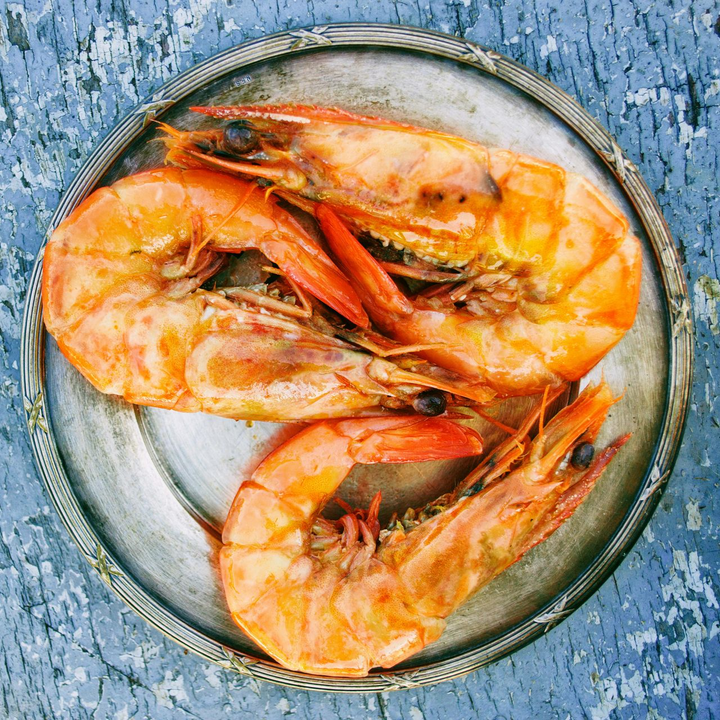 三隻熟蝦放在銀盤上，背景是藍色的木質。