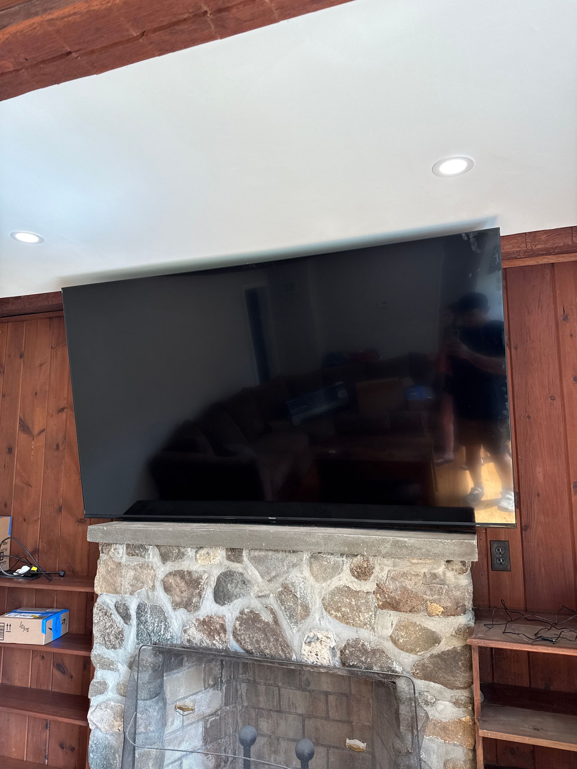 Large flat-screen TV mounted above a stone fireplace in a wood-paneled room