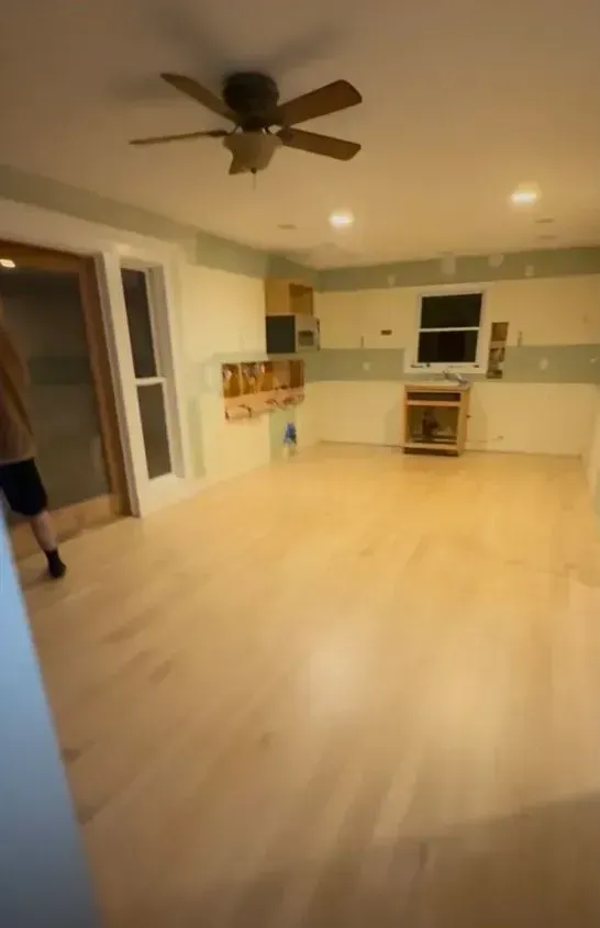 Empty living room and kitchen with light wood floors, ceiling fan, and recessed lights.