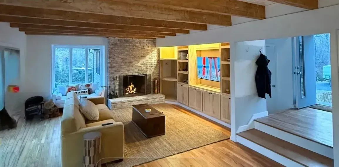Bright living room with wood beams, stone fireplace, yellow built-ins, white sofa, and a window seat.