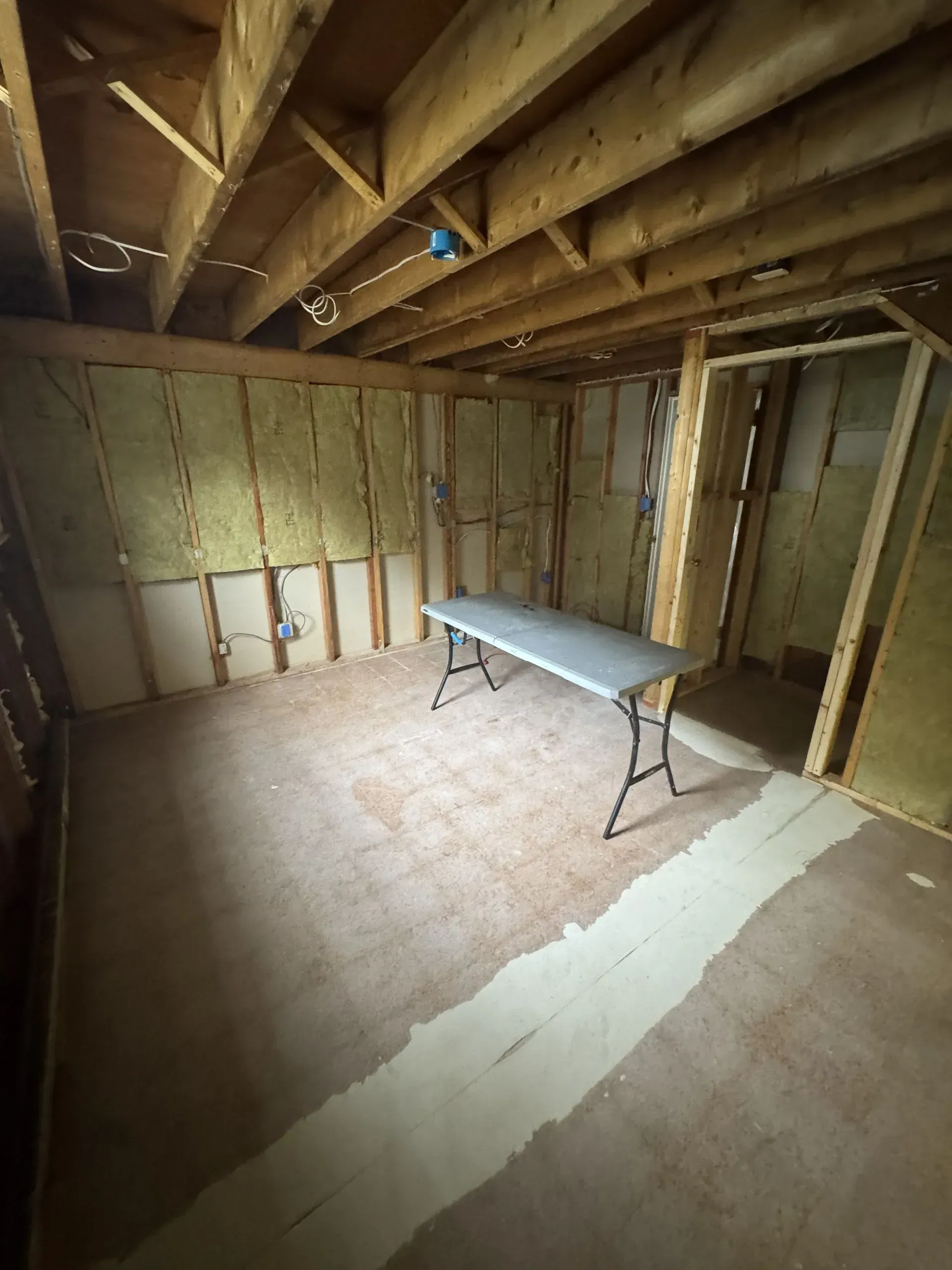 Unfinished basement room with exposed studs, tiled floor, and a folding table in the center.
