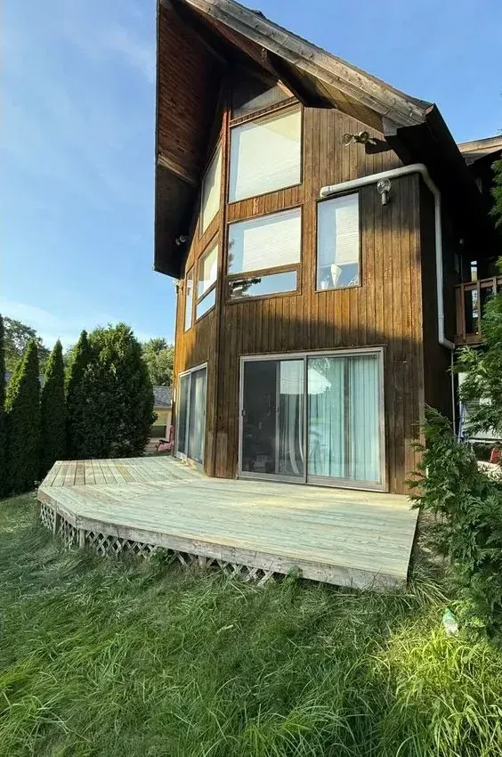Modern wooden house with large windows and a curved deck in a grassy yard
