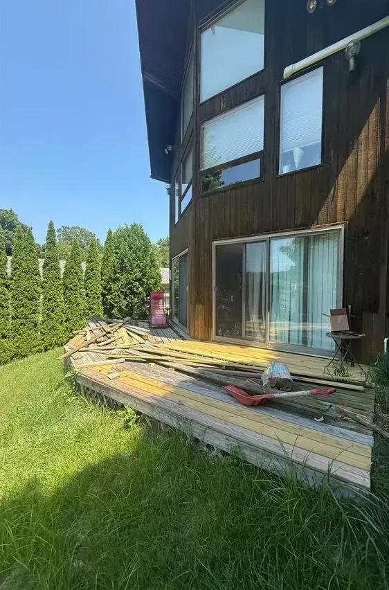House exterior with wooden deck under construction, boards and tools on a sunny lawn